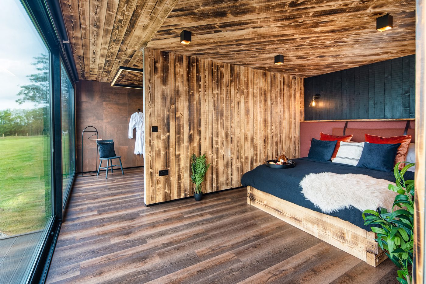 Rusty Boathouse bedroom — king-size bed with velvet headboard, timber walls and lake view