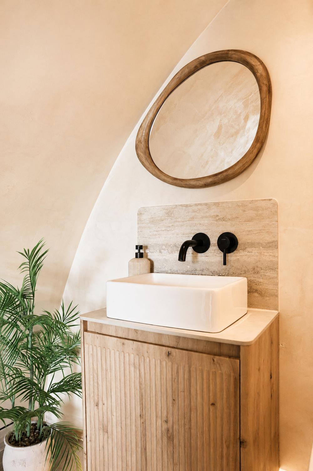 Bathroom vanity beside a potted palm, with round mirror overhead