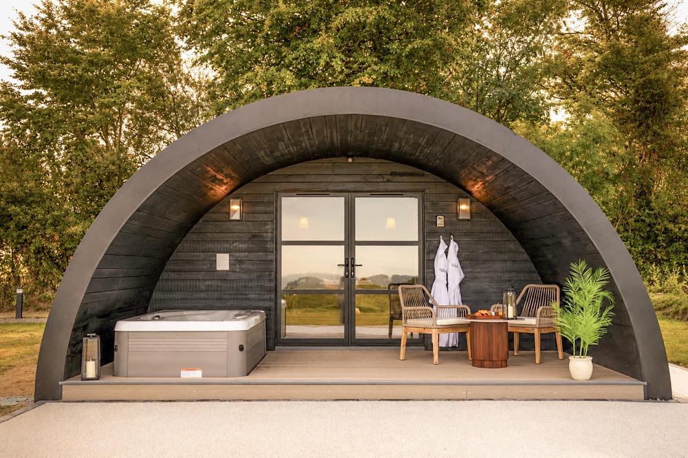 The Hog Hut's barrel-arch exterior at golden hour, hot tub and deck beneath the curve